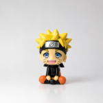 Cute Naruto Uzumaki chibi PVC mini figure sitting down with blonde spiky hair, Leaf Village headband, blue eyes, orange and black outfit, and smiling expression on a white background.