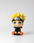 Cute Naruto Uzumaki chibi PVC mini figure sitting down with blonde spiky hair, Leaf Village headband, blue eyes, orange and black outfit, and smiling expression on a white background.